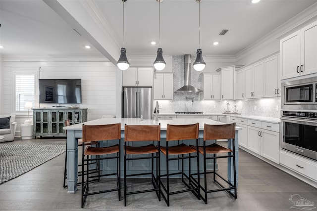 kitchen featuring a breakfast bar, a center island with sink, stainless steel appliances, and wall chimney exhaust hood