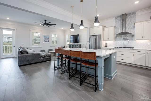 kitchen with a breakfast bar area, high end refrigerator, a kitchen island with sink, gas stovetop, and wall chimney range hood