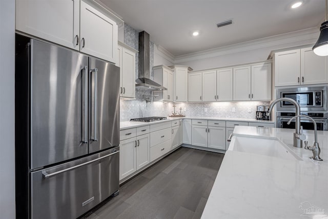 kitchen with appliances with stainless steel finishes, wall chimney exhaust hood, backsplash, and light stone counters