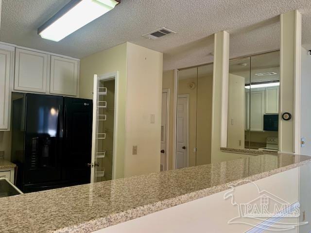 kitchen with light stone counters, a textured ceiling, black appliances, and white cabinets