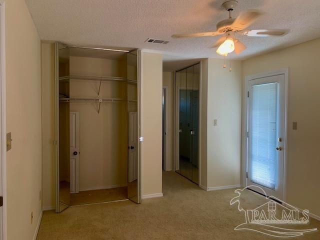 unfurnished bedroom with light carpet, a textured ceiling, a closet, and ceiling fan