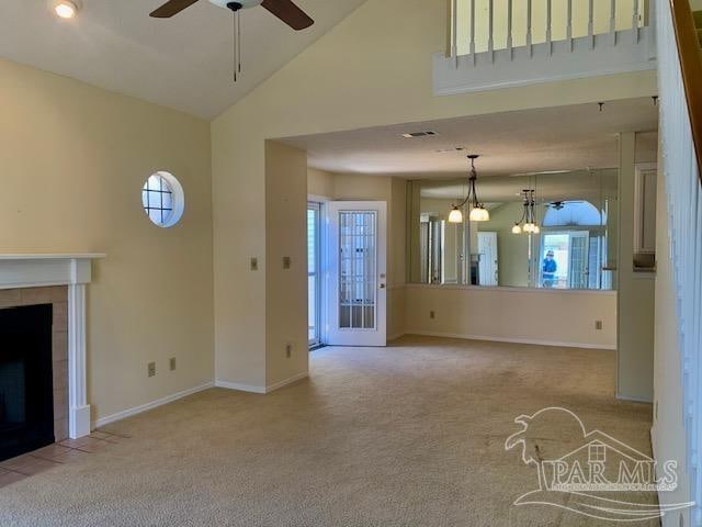 unfurnished living room with light colored carpet, a tile fireplace, ceiling fan with notable chandelier, and high vaulted ceiling