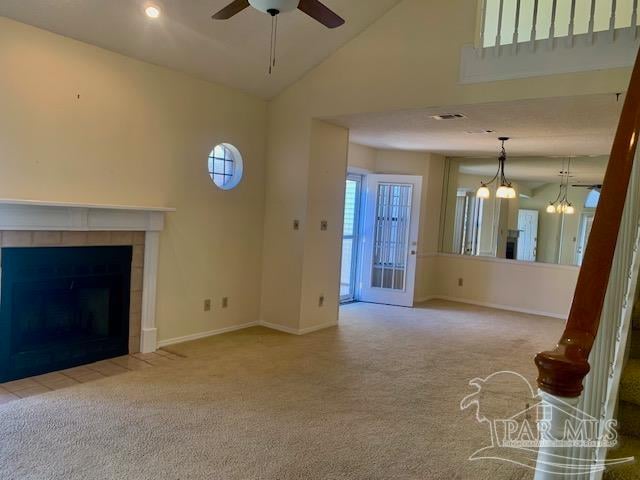 unfurnished living room featuring high vaulted ceiling, a tiled fireplace, ceiling fan with notable chandelier, and light colored carpet