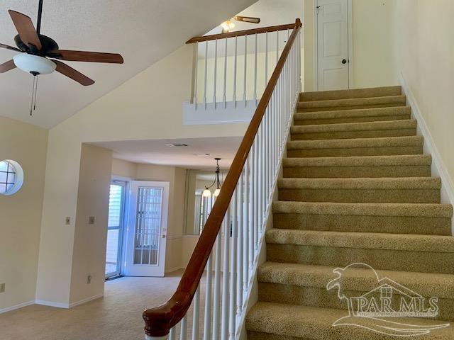 staircase featuring carpet, ceiling fan, and a high ceiling