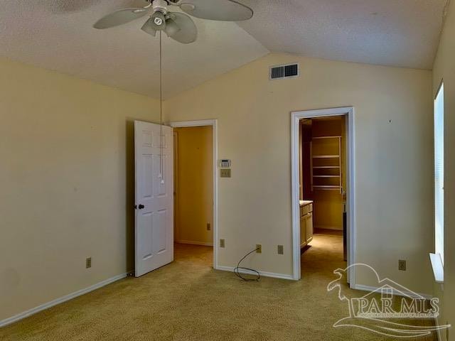 unfurnished bedroom with a spacious closet, a textured ceiling, lofted ceiling, carpet flooring, and ceiling fan