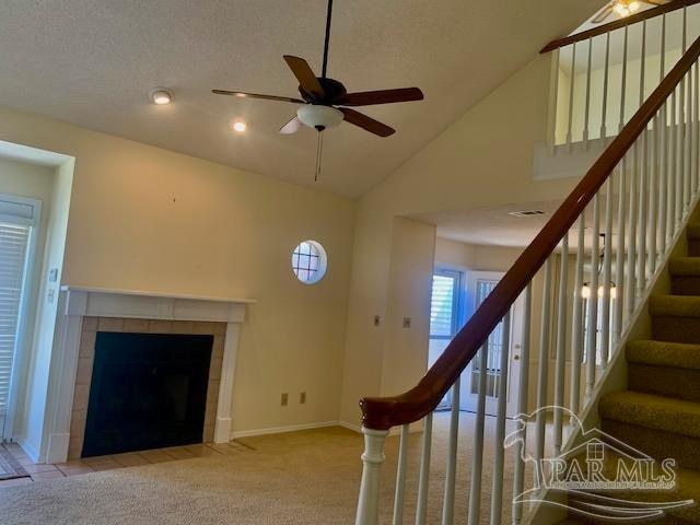 interior space with ceiling fan, carpet flooring, a tiled fireplace, and high vaulted ceiling