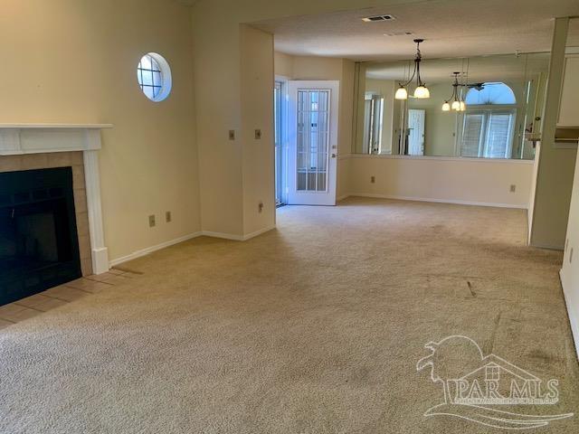 unfurnished living room featuring a tile fireplace, light carpet, and a notable chandelier