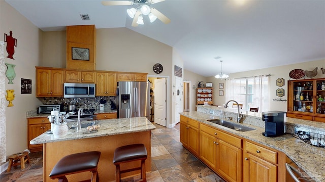 kitchen featuring a breakfast bar, stainless steel appliances, a kitchen island with sink, sink, and decorative light fixtures