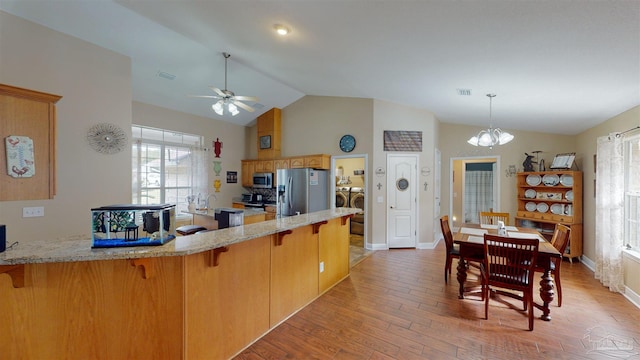 kitchen featuring ceiling fan with notable chandelier, vaulted ceiling, washing machine and dryer, light wood-type flooring, and appliances with stainless steel finishes