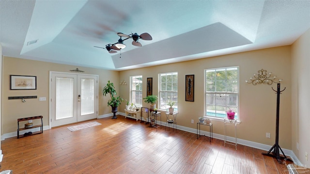 interior space with ceiling fan, wood-type flooring, french doors, and a tray ceiling