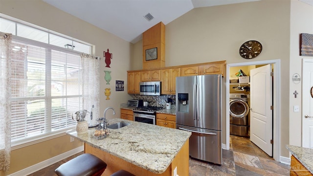 kitchen with a center island with sink, sink, light stone countertops, washer / dryer, and stainless steel appliances