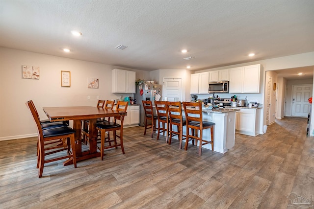 kitchen with light wood-type flooring, a breakfast bar, appliances with stainless steel finishes, a center island with sink, and white cabinets