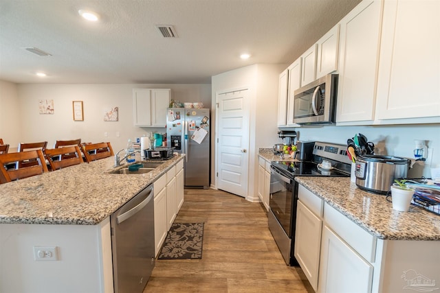 kitchen featuring white cabinets, light wood-type flooring, stainless steel appliances, sink, and an island with sink