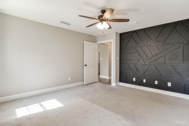 unfurnished room featuring ceiling fan, a decorative wall, light carpet, visible vents, and baseboards