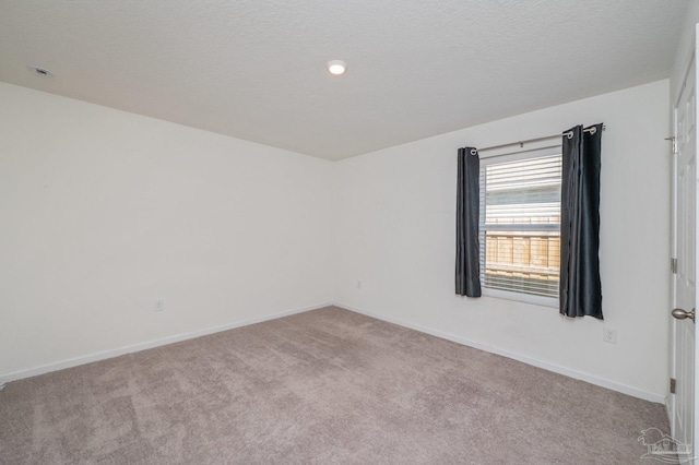 spare room featuring light colored carpet, a textured ceiling, and baseboards