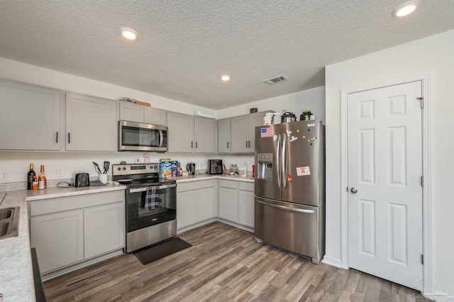 kitchen featuring a textured ceiling, wood finished floors, light countertops, appliances with stainless steel finishes, and gray cabinets