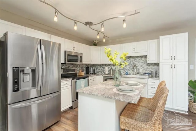 kitchen with sink, white cabinetry, a kitchen breakfast bar, a kitchen island, and appliances with stainless steel finishes