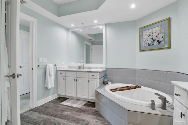 bathroom featuring wood finished floors, a bath, vanity, and recessed lighting