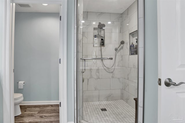 bathroom featuring a shower stall, toilet, wood finished floors, and baseboards