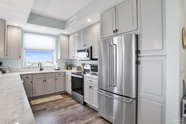 kitchen with appliances with stainless steel finishes, a sink, wood finished floors, light stone countertops, and recessed lighting