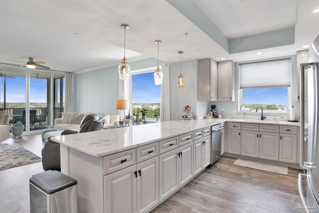 kitchen featuring stainless steel appliances, a peninsula, a sink, a ceiling fan, and light stone countertops