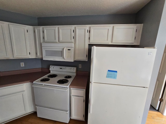 kitchen featuring white appliances, white cabinetry, hardwood / wood-style floors, and a textured ceiling