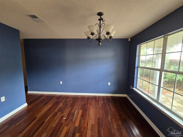 spare room with a textured ceiling, an inviting chandelier, and dark wood-type flooring