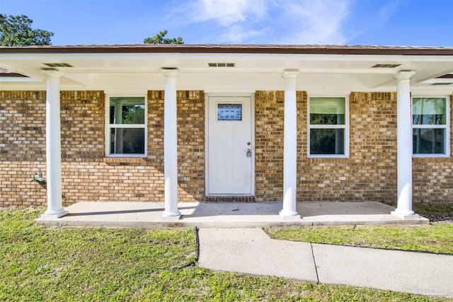 doorway to property featuring covered porch, brick siding, and visible vents