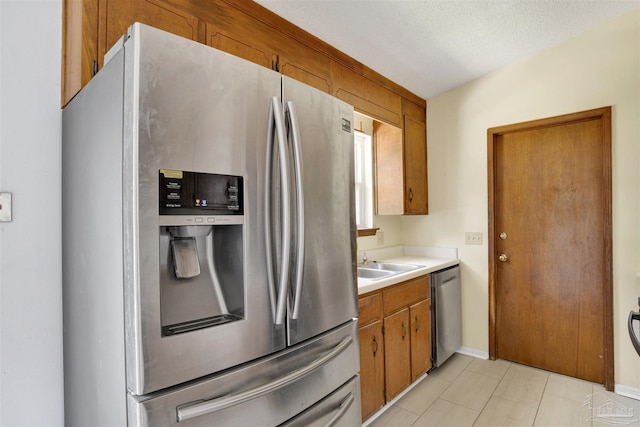 kitchen featuring stainless steel appliances, a sink, baseboards, light countertops, and brown cabinets