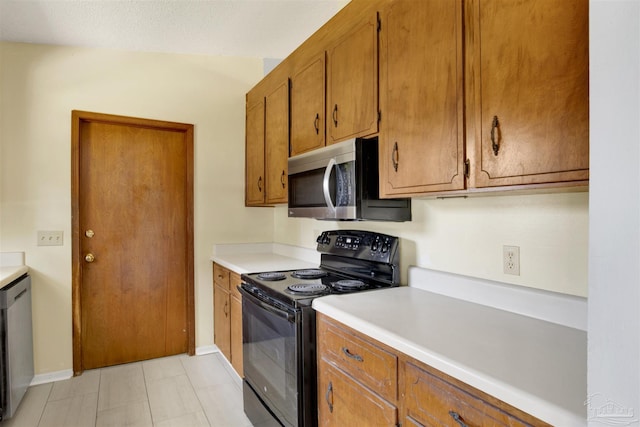 kitchen with baseboards, light countertops, appliances with stainless steel finishes, and brown cabinets