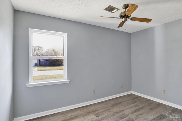 empty room featuring a textured ceiling, dark wood-style flooring, a ceiling fan, visible vents, and baseboards