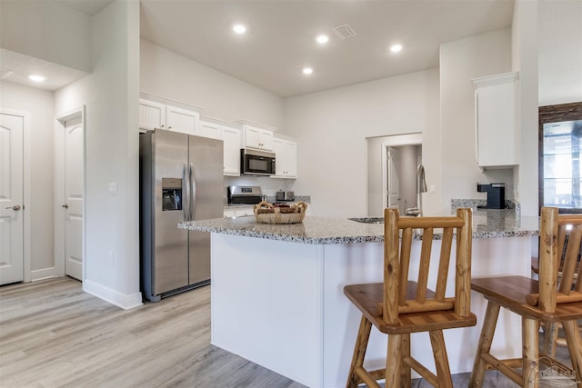 kitchen featuring light stone countertops, a peninsula, stainless steel appliances, light wood-style floors, and white cabinetry