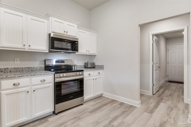 kitchen with light stone counters, baseboards, light wood-style flooring, appliances with stainless steel finishes, and white cabinetry