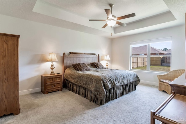 bedroom with light colored carpet, a raised ceiling, and baseboards