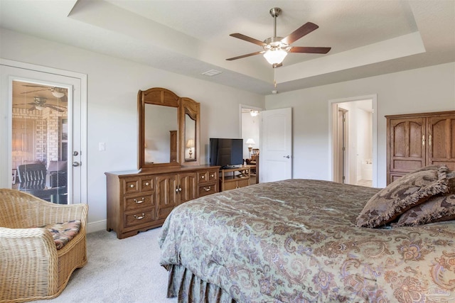 bedroom with baseboards, light colored carpet, a tray ceiling, ensuite bathroom, and a ceiling fan