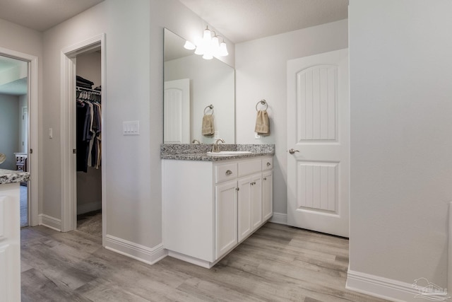 bathroom with vanity, a walk in closet, baseboards, and wood finished floors