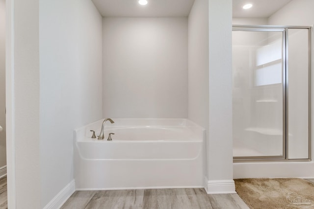 bathroom with a bath, a stall shower, baseboards, and wood finished floors