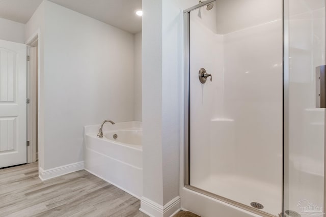 full bathroom featuring a bath, a stall shower, baseboards, and wood finished floors