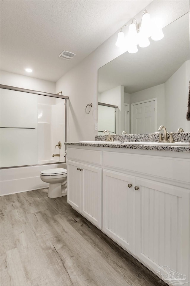 bathroom with visible vents, bath / shower combo with glass door, toilet, double vanity, and wood finished floors