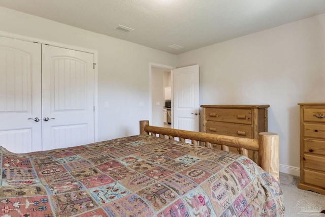 bedroom with a closet, visible vents, light colored carpet, and a textured ceiling