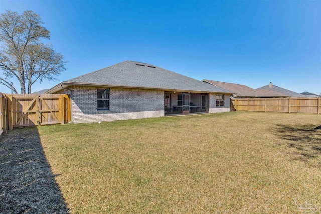 back of house with a gate, a yard, a fenced backyard, a sunroom, and brick siding