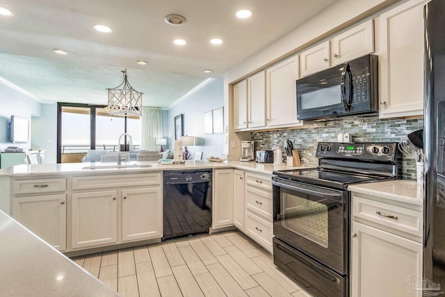 kitchen with white cabinetry, sink, an inviting chandelier, kitchen peninsula, and black appliances