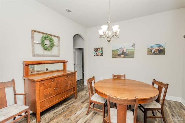 dining area featuring arched walkways, visible vents, light wood-style flooring, an inviting chandelier, and baseboards