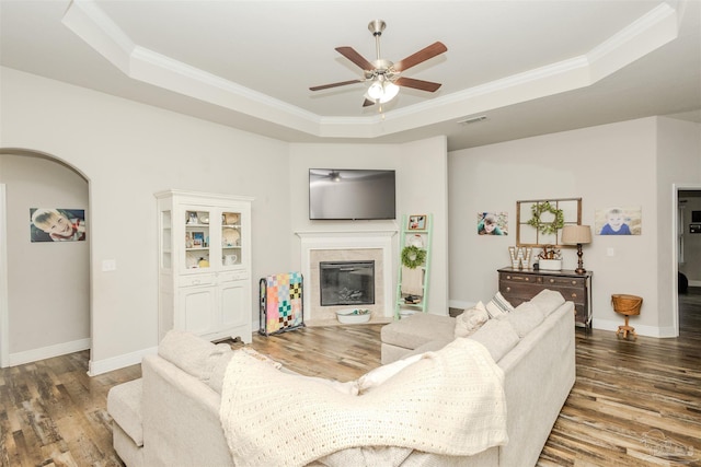 living area with arched walkways, wood finished floors, a raised ceiling, and visible vents