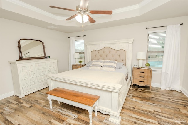 bedroom featuring baseboards, ornamental molding, a raised ceiling, and light wood-style floors