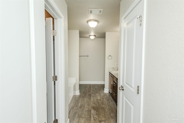 corridor with dark wood-style flooring, visible vents, and baseboards