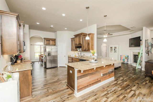 kitchen featuring light stone counters, arched walkways, stainless steel refrigerator with ice dispenser, a sink, and a peninsula