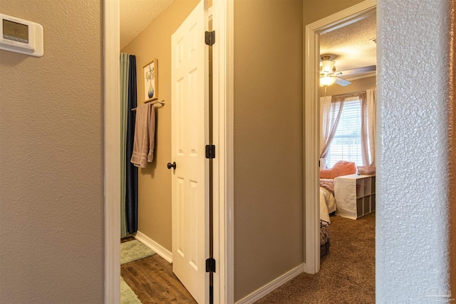 corridor with a textured wall, a textured ceiling, and baseboards