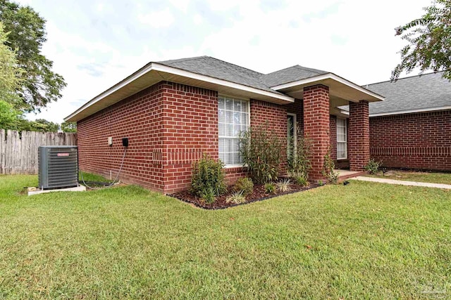 view of side of home with central air condition unit, brick siding, fence, roof with shingles, and a lawn