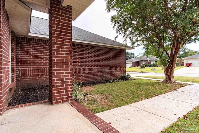 view of side of property featuring a yard, roof with shingles, brick siding, and a chimney